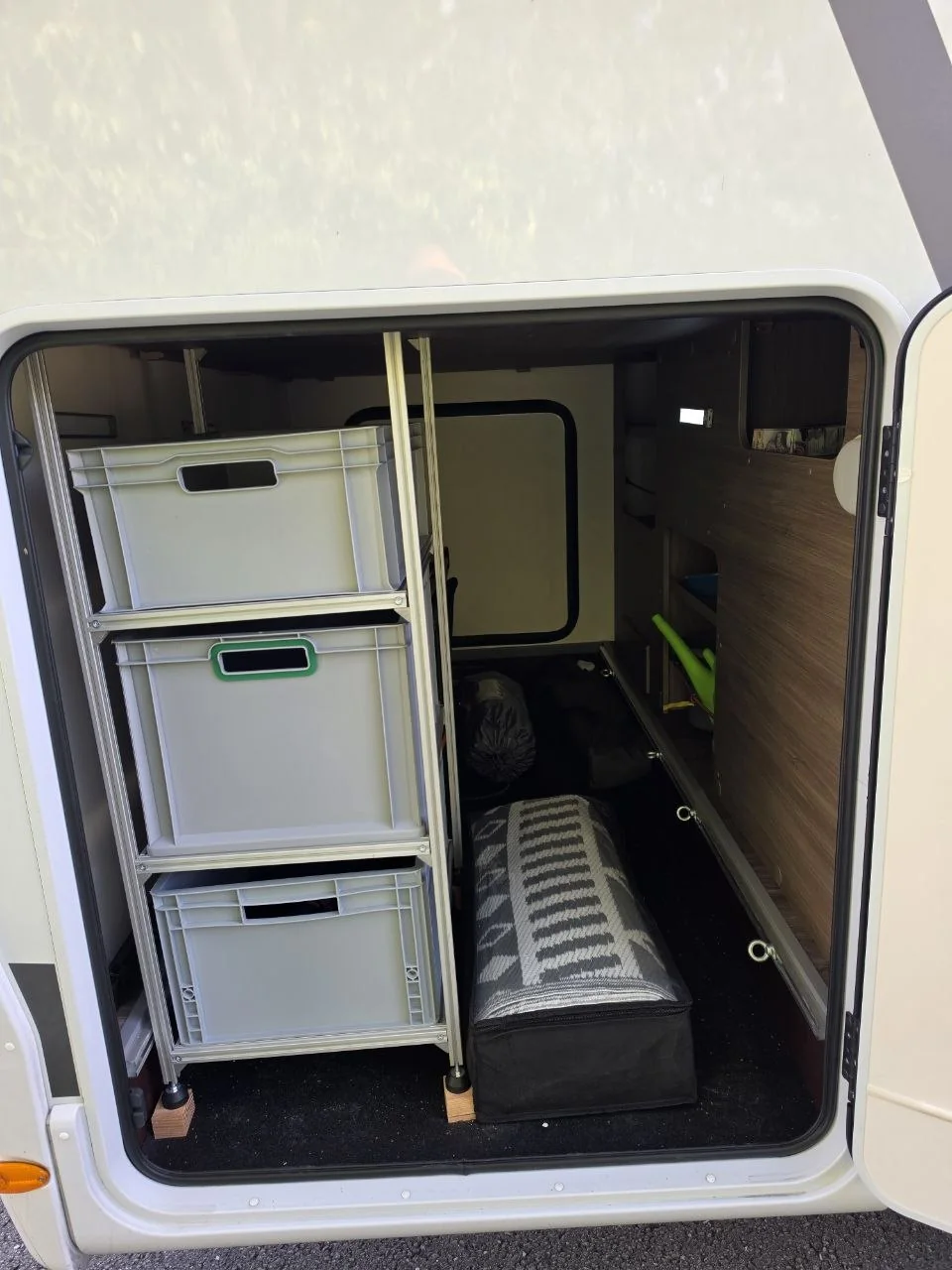 Wohnmobil-Heckgarage mit drei grauen Aufbewahrungsboxen im Metallregal und Gepäck daneben.